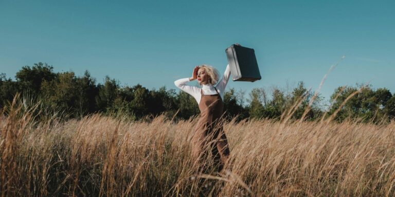 Sustainable travel: photo of a woman with suitcase in wild field